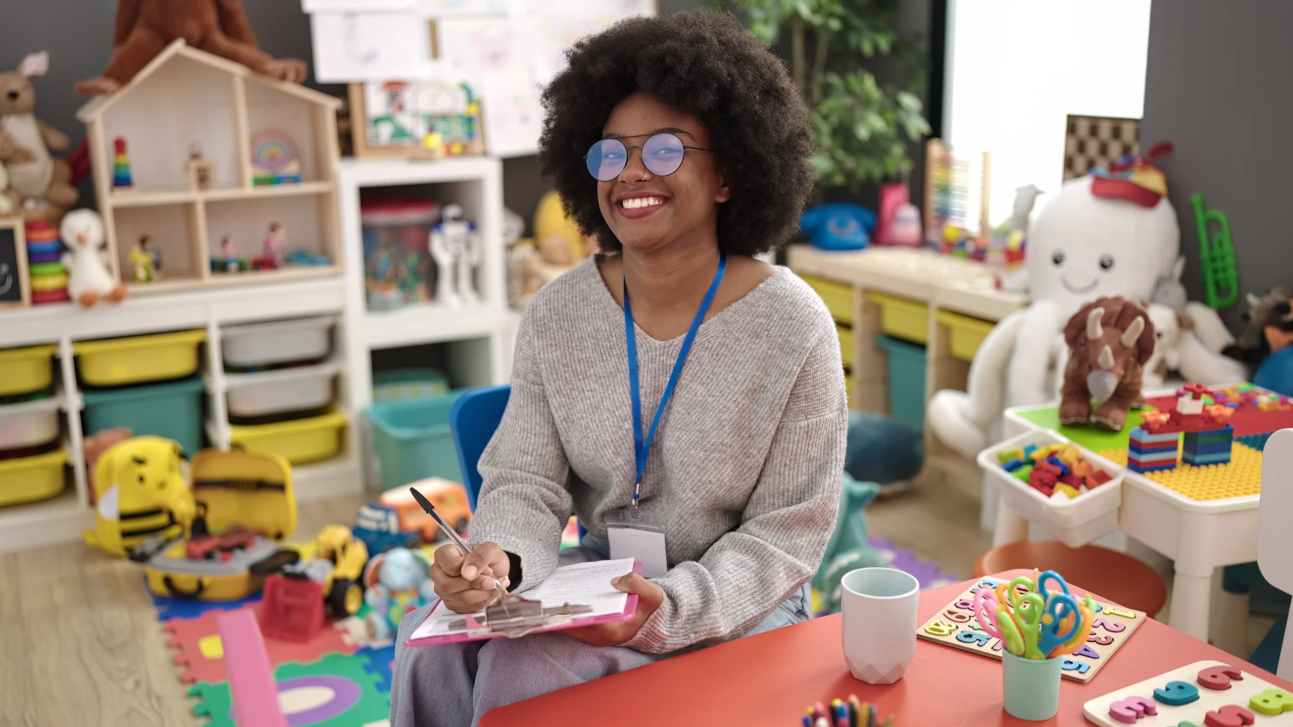 African american woman preschool teacher smiling confident writing on document at kindergarten