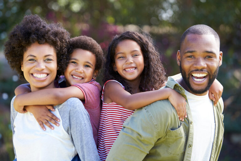 Portrait Of Parents Giving Children Piggybacks In Garden